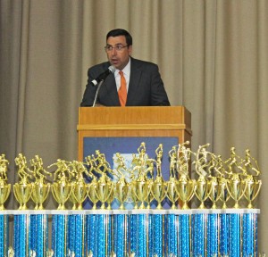 Athletic Director Mike McCleary speaks at Athletic Awards Night. In the foreground are the many trophies to present.